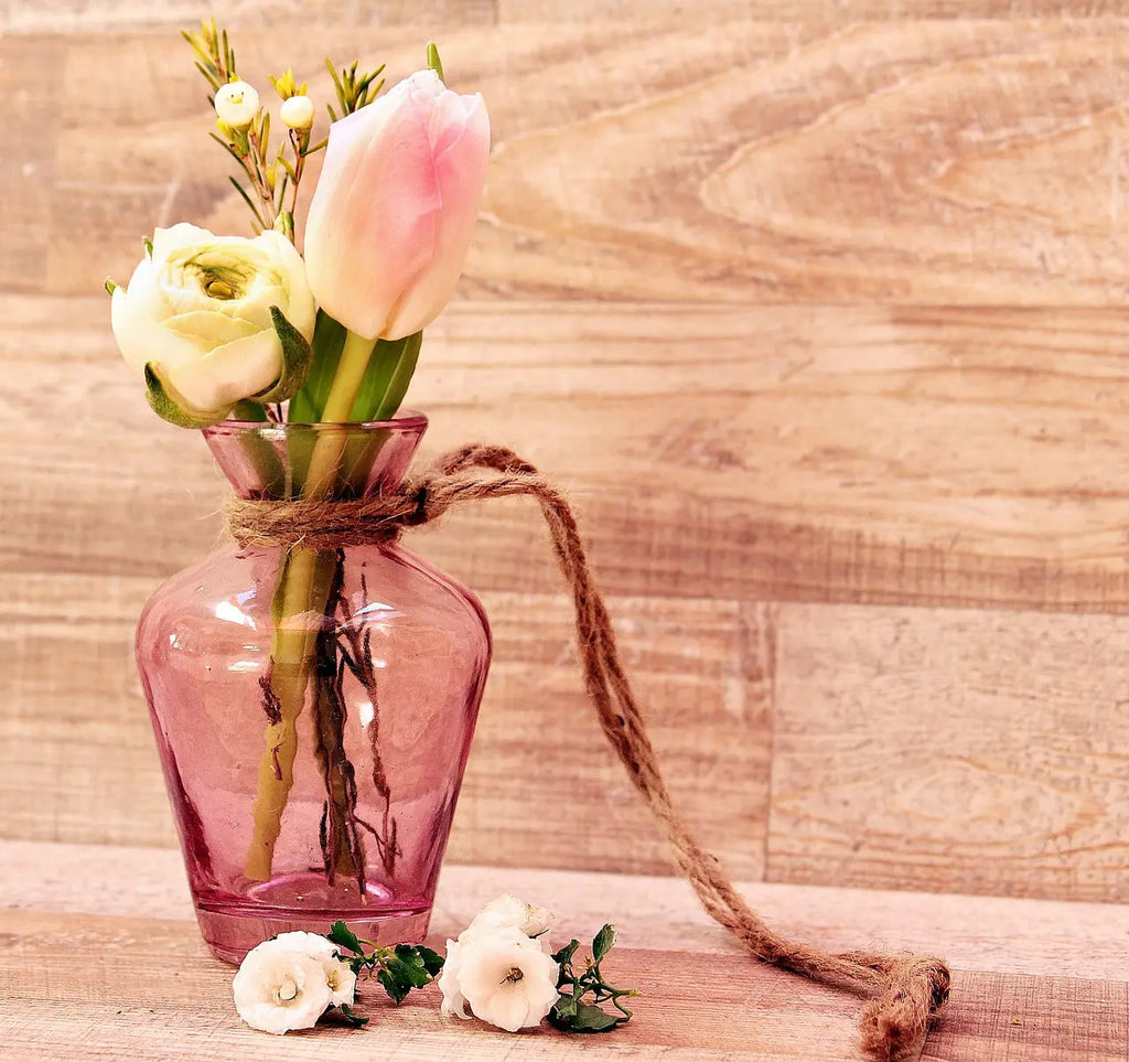 Vase rose transparent ornée de fleurs fraiches et décorée d'une ficelle