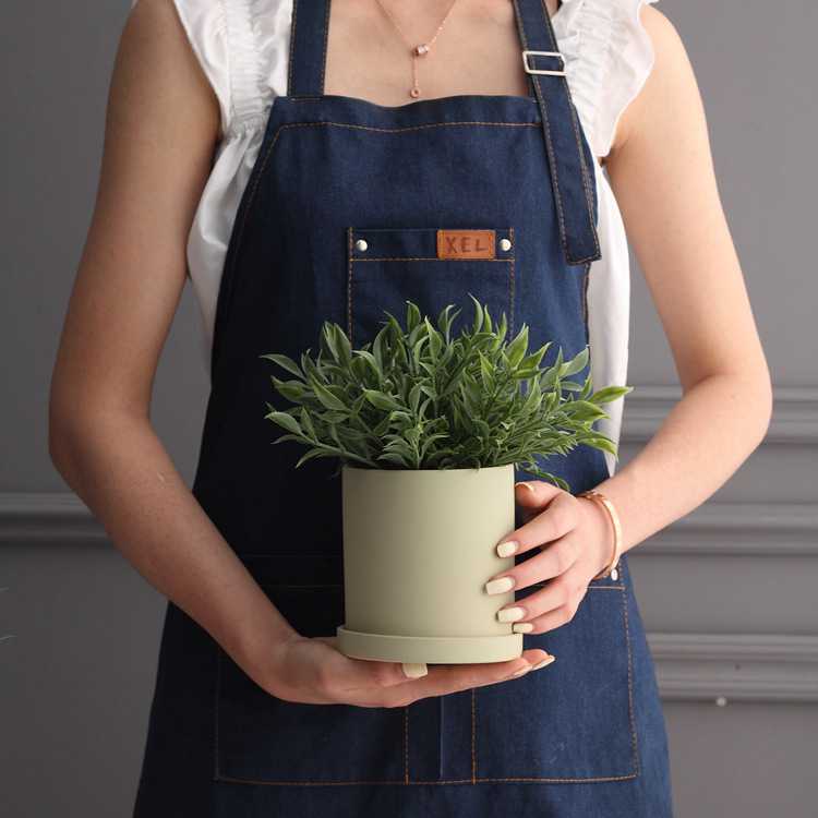 Femme en tenue de jardinage portant une plante dans un pot de fleur verre.